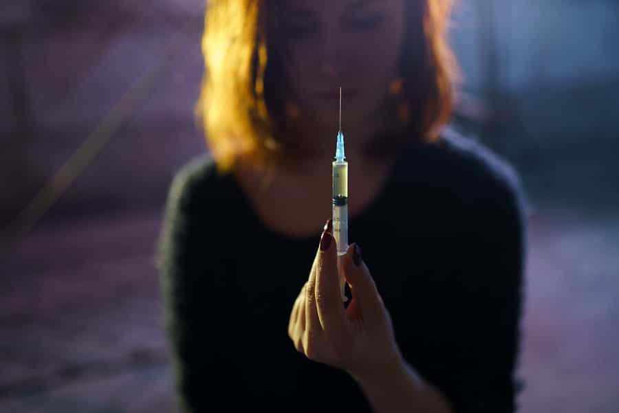 A young woman holding up a heroin needle.