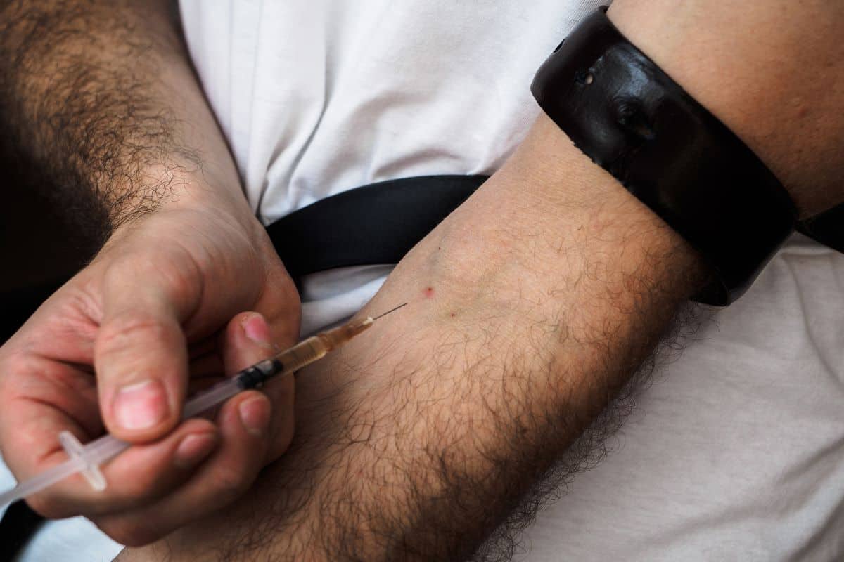 A close up of a man about to inject his arm with a heroin needle.