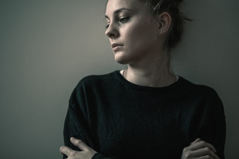 A woman with an anxiety disorder leaning up against a wall.