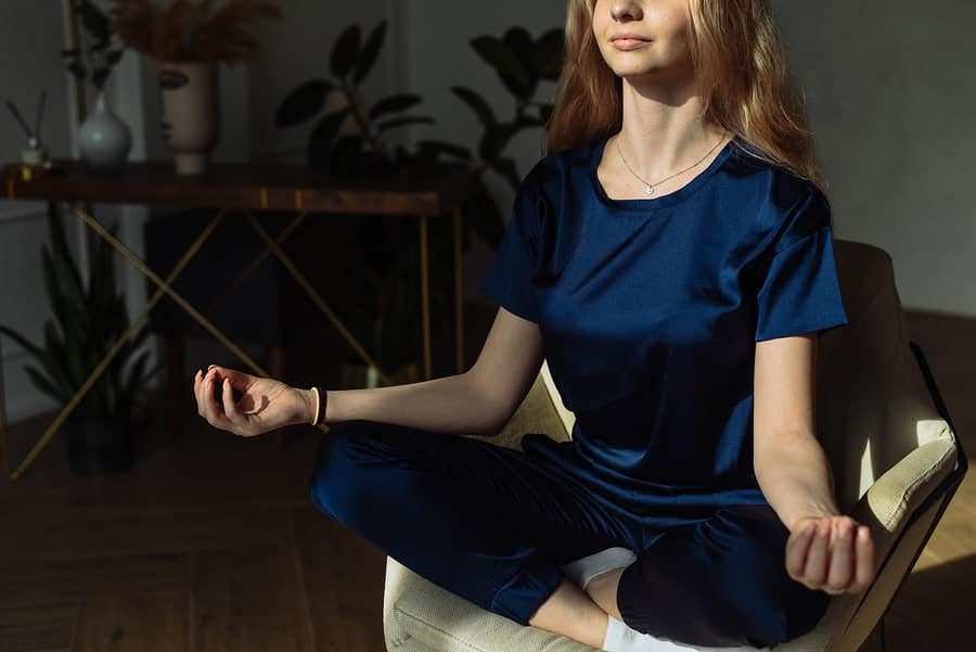 A young woman in recovery meditating on an armchair at home.