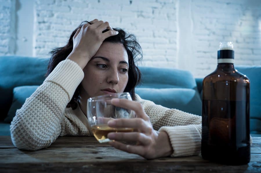 A woman struggling with alcohol addiction drinking at home.